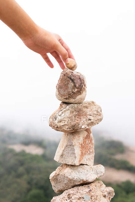 Anonyme Touristin legt Stein in Haufen, während sie bergiges Terrain mit Nebel erkundet — Stockfoto