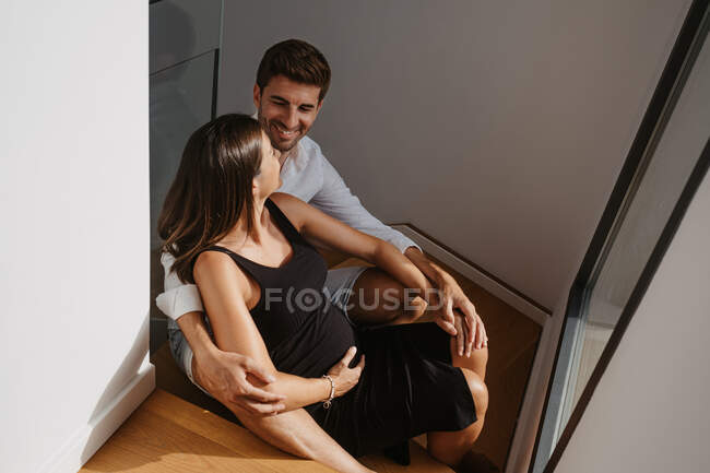 From above of content male embracing expectant female partner while conversing and looking at each other on floor at home — Stock Photo