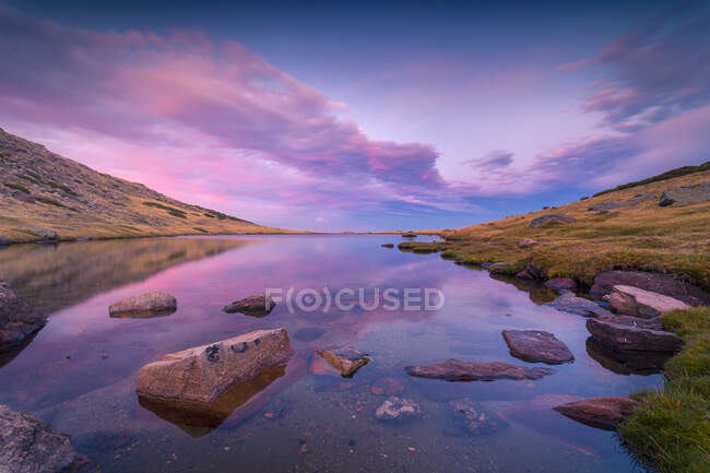 Pintoresco paisaje de río tranquilo con rocas situadas en las tierras altas de la Sierra de Guadarrama en España bajo el colorido cielo al amanecer - foto de stock