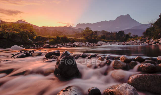 Неповторні краєвиди бурхливої річки, що тече на валунах, оточені зеленими рослинами в гірській місцевості під час заходу сонця в Малайзії. — стокове фото