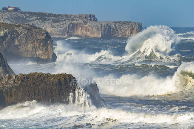 Desde arriba espectacular paisaje de poderosas olas marinas espumosas salpicando cerca de escarpados acantilados rocosos con cuevas en Pria Asturias España - foto de stock