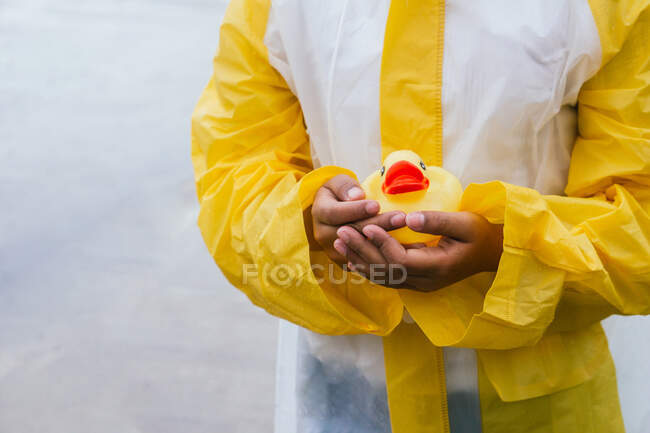 Crop kid in slicker with wet hair and rubber duck on grey background — Stock Photo