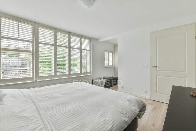 Lit douillet confortable avec couette blanche placée près de grandes fenêtres dans la chambre moderne dans l'appartement — Photo de stock