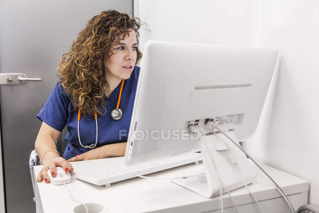 Mujer en uniforme médico escribiendo en el teclado de la computadora mientras trabaja en la clínica de salud - foto de stock