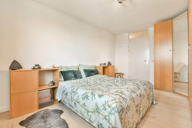 Diseño creativo de dormitorio con cama contra armario de madera sobre parquet con alfombra en casa - foto de stock