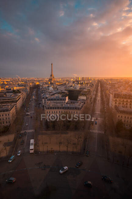 Drone vista de fachadas de casas urbanas y carreteras con transporte bajo el cielo nublado brillante al atardecer en París Francia - foto de stock