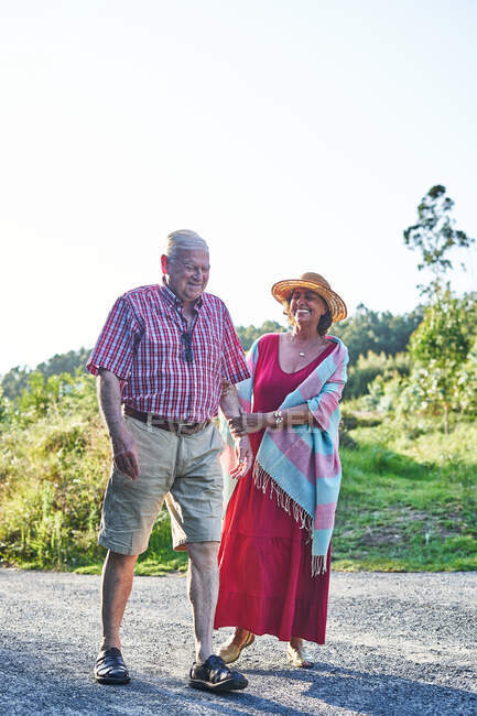 Full body of laughing old couple enjoying walk together in rural area with green plants — Stock Photo