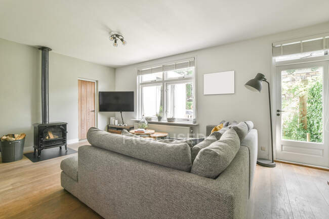 Divano grigio con cuscini e TV in elegante soggiorno in appartamento di lusso durante il giorno — Foto stock
