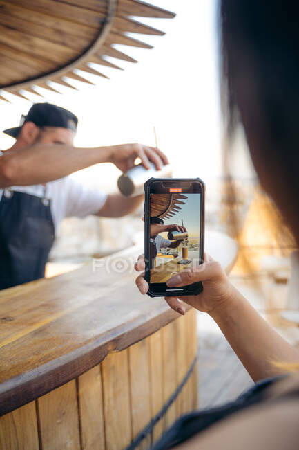 Crop anonymous female customer shooting video of bartender mixing cocktail in bar while waiting order — Stock Photo