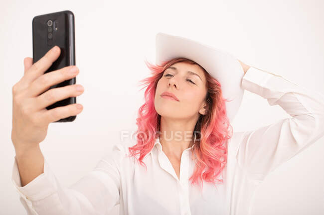 Frontansicht fröhliche Frau mit pinkfarbenen Haaren in stylischer Kleidung macht Selfie auf Smartphone vor hellem Hintergrund — Stockfoto