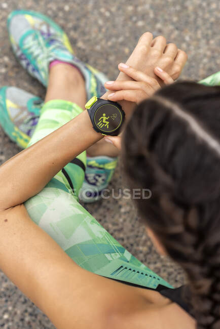 Зверху анонімні жінки-бігуни перевіряють імпульс на сучасному вживаному фітнес-браслеті під час тренувань у місті — стокове фото