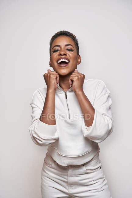 Positivo jovem afro-americano feminino em vestuário elegante com maquiagem e cabelo curto no fundo claro — Fotografia de Stock