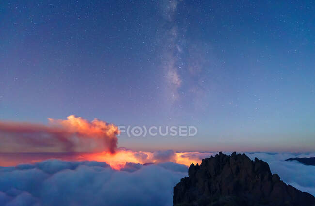 Vertical milky way and volcano smoke over a sea of bluish clouds below high peaks on a starry night. Cumbre Vieja volcanic eruption in La Palma Canary Islands, Spain, 2021 — Stock Photo
