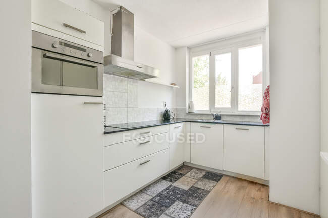 Interieur der stilvollen Küche mit weißen Schränken und buntem Teppich auf Parkett in der Wohnung tagsüber — Stockfoto
