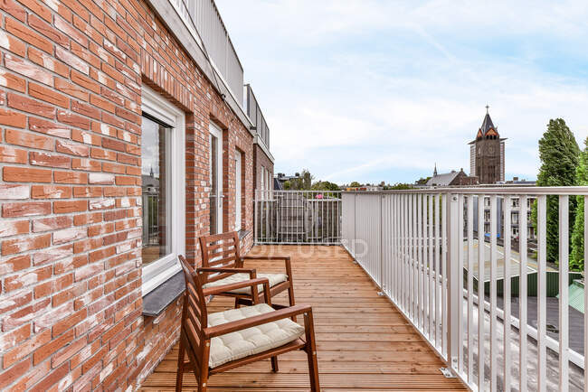 Holzstühle auf Balkon mit Metallzaun von Wohnhaus aus Ziegelsteinen platziert — Stockfoto