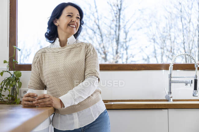 Mature confident woman standing looking away in kitchen near countertop holding mug of hot beverage in the morning at home — Stock Photo