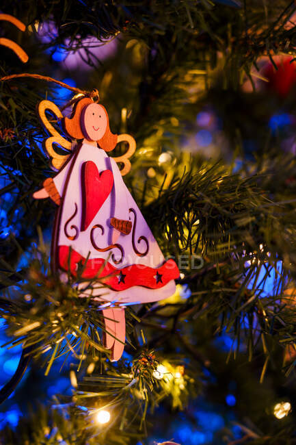 Angelo e decorazioni a forma di stella appese ai rami di abete artificiale di Natale incandescente di notte — Foto stock