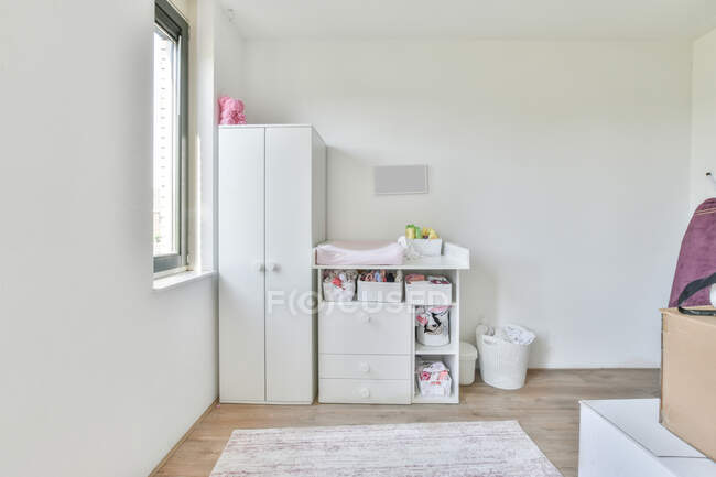 Минималистичный интерьер светлой комнаты с белым шкафом и шкафом с полками, расположенными возле окна в дневное время — стоковое фото