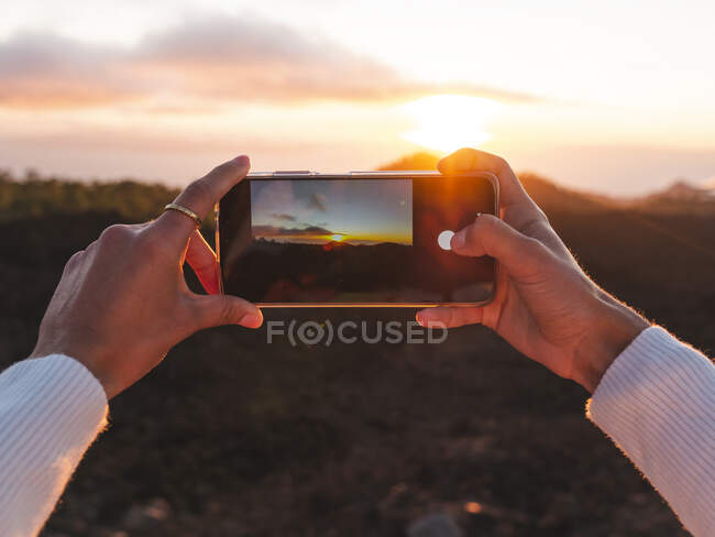 Crop unrecognizable tourist taking photo of ocean and mountain on cellphone at sunset in Tenerife Canary Islands Spain — Stock Photo