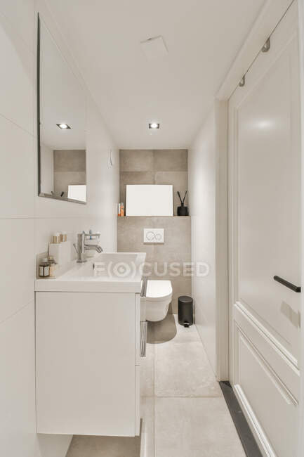 Waschtisch mit Toilettenartikeln unter Spiegel gegen Toilettenschüssel und Mülleimer auf Fliesenboden im modernen Badezimmer — Stockfoto
