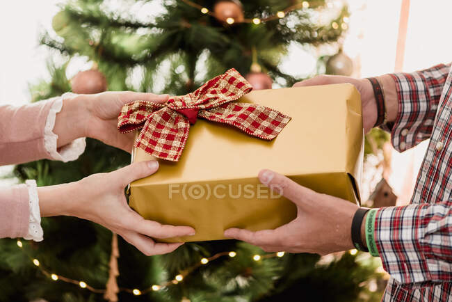 Cosecha anónima mujer pasando presente caja con arco a marido durante las vacaciones de Año Nuevo en casa - foto de stock