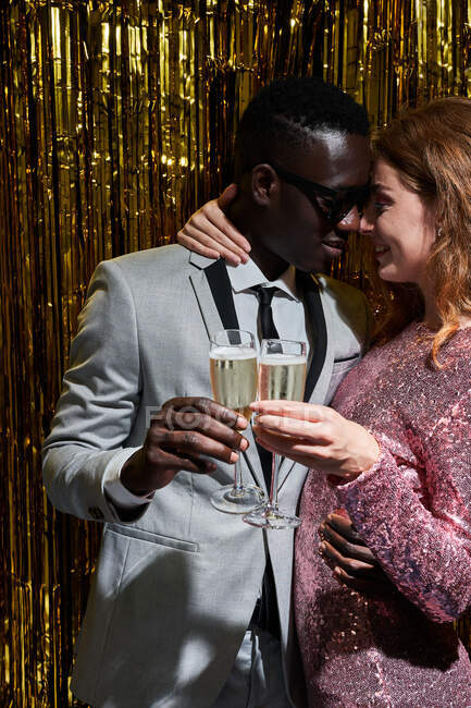 Cortar sincera jovem mulher abraçando namorado preto elegante enquanto clica copos de champanhe durante a celebração de Ano Novo — Fotografia de Stock