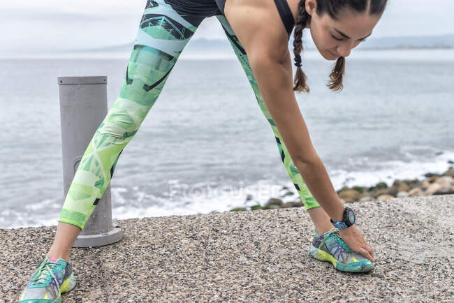 Flexible Läuferin bei Vorwärtsbeugeübungen und Streckung der Beine beim Training am Damm im Sommer — Stockfoto