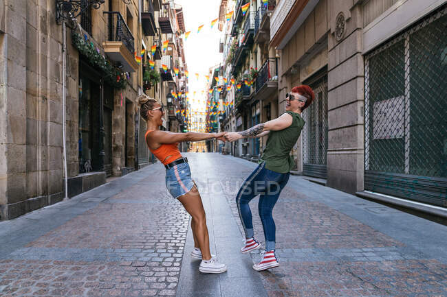 Вид збоку на щасливу молоду гомосексуальну пару з татуюваннями в модному одязі, дивлячись один на одного, розважаючись на вулиці — стокове фото