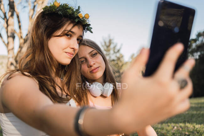 Female teens taking self portrait on cellphone in sunny park on blurred background — Stock Photo