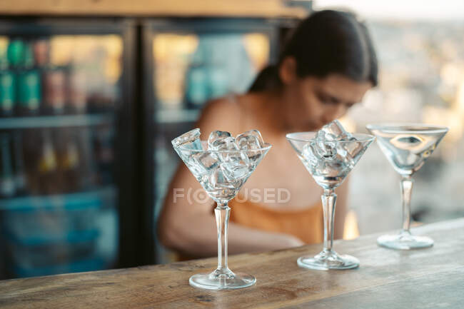 Occupato barista donna che lavora al bancone con fila di bicchieri con cubetti di ghiaccio nel bar — Foto stock