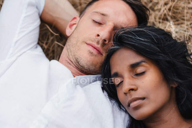 From above of crop unshaven man with Indian female partner sleeping on meadow in daytime — Stock Photo