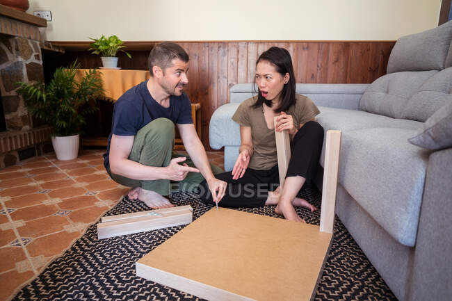 Vielrassiges Paar stellt Tisch auf Teppich im Haus zusammen — Stockfoto