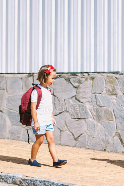 Side view of schoolchild with backpack on pavement looking forward in sunlight — Stock Photo