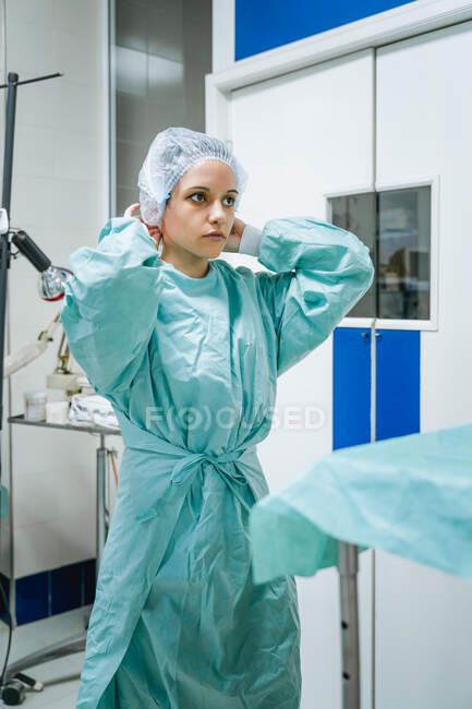 Young female veterinary surgeon in green uniform putting on disposable cap while looking forward in clinic — Stock Photo