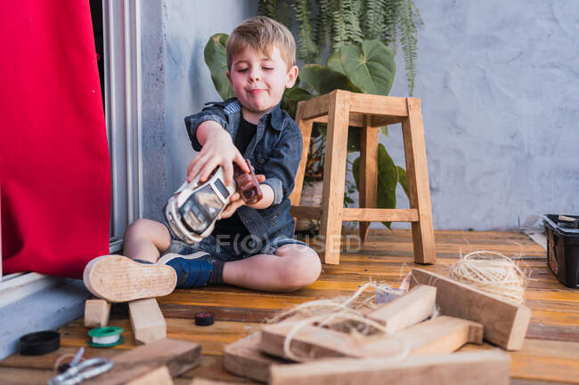 Criança encantadora sorrindo enquanto brincava com automóveis de brinquedo entre peças de madeira e banquinho artesanal à luz do dia — Fotografia de Stock