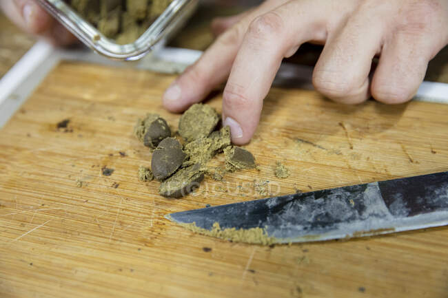 Ernte unkenntlich Männchen mit Messer zerkleinert getrocknete Cannabispflanze Stück auf Holzbrett in Arbeitsraum — Stockfoto