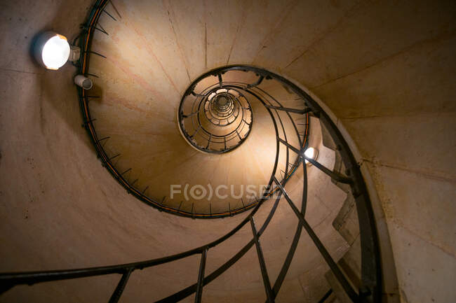 Top view of aged curved staircase with railing and lamps on rough wall in building — Stock Photo