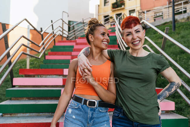 Trendy felici donne omosessuali abbracciano guardando l'un l'altro mentre scende le scale contro le case urbane — Foto stock