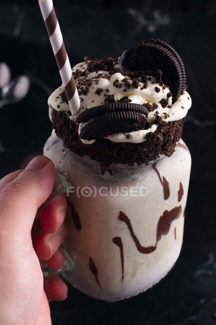 Crop anonymous person with tasty shake with whipped cream and chocolate cookies on top of jar — Stock Photo