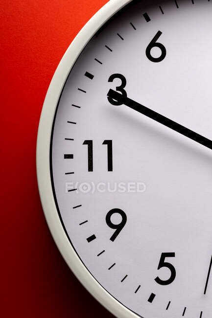 Round shaped minimalistic clock with numbers and arrows on colorful red background — Stock Photo
