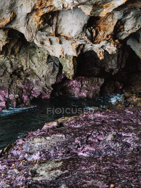 Agua de mar transparente y ondulada que fluye a través de una cueva rocosa áspera con salientes irregulares afilados - foto de stock