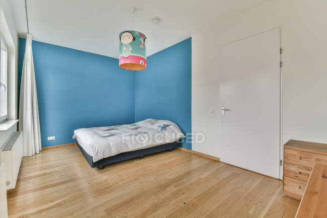 Cover on bed against commode on parquet under lamp with cartoon character illustration in modern bedroom — Stock Photo