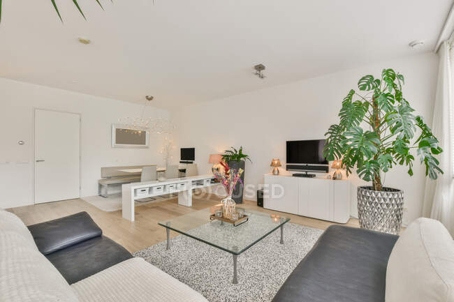 Diseño creativo de habitación espaciosa con mesas y sofá en parquet en casa con lámpara de araña y balcón - foto de stock