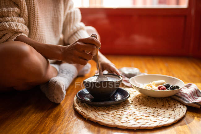 Crop anonymous female sitting with crossed legs and eating sweet sliced bananas blueberry and raspberries — Stock Photo