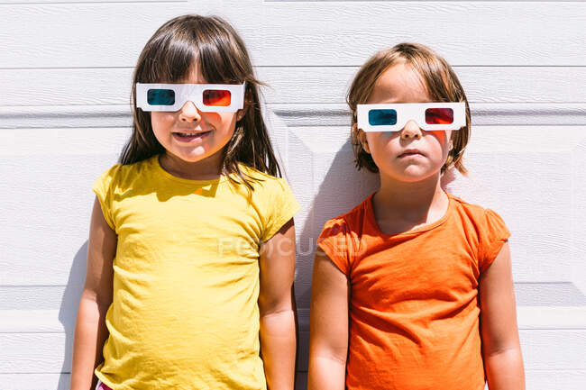 Cheerful cute girls in casual colorful clothes and three dimensional glasses standing on white wall background — Stock Photo