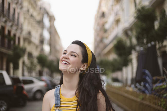 Молодая счастливая женщина с длинными каштановыми волосами, в джинсах, гуляет по улице, смотрит в камеру с улыбкой — стоковое фото