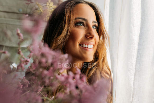 Portrait de magnifique adolescente à la maison derrière des fleurs colorées et détournant les yeux — Photo de stock