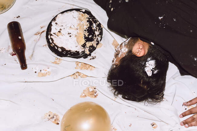 Зверху п'яний самець спить біля розбитого торта на день народження і порожньої пляшки під час вечірки. — стокове фото