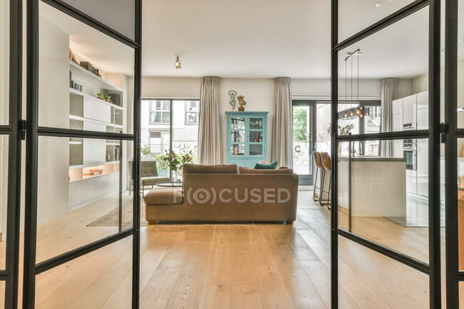 Attraverso vetro di porta su divani in camera spaziosa con cucina moderna con zona pranzo e chitarra — Foto stock