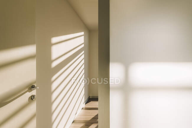 Interior of door handle in empty spacious loft hallway with geometrical shadows and sunlight on white walls — Stock Photo